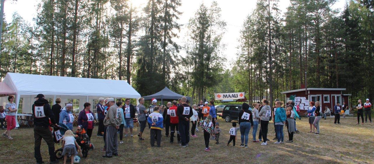 Kyläläisiä kokoontuneena ulkotapahtumaan metsämaisemassa